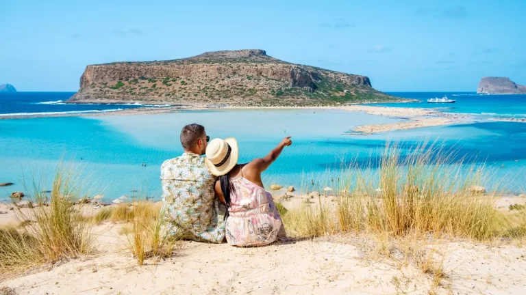 Kreeta Kreikka, Balosin laguuni Kreetan saari, Kreikka. Matkailijat rentoutuvat Balosin rannan kristallinkirkkaassa meressä. pari miestä ja nainen käyvät rannalla lomalla Kreikassa aurinkoisena päivänä.