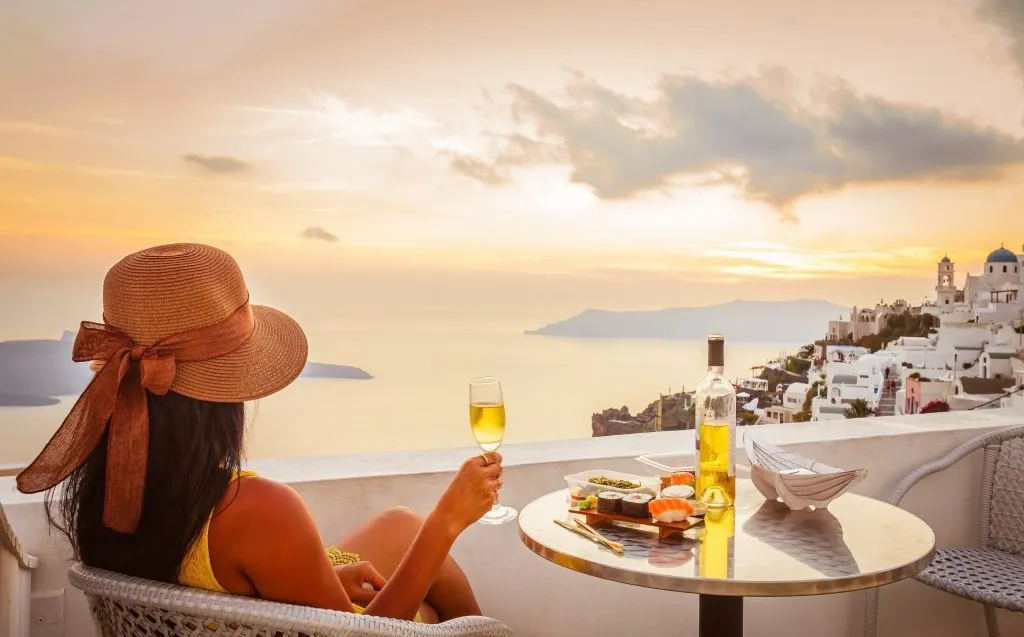 Weibliche Touristin genießt Essen, Wein und den Blick auf den Sonnenuntergang auf Santorin, Griechenland