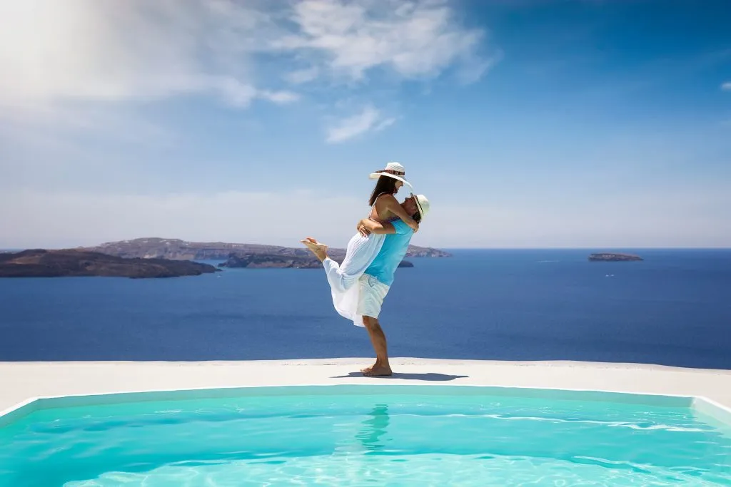 Et lykkelig sommerferiepar står og omfavner et svømmebasseng med utsikt over Middelhavet.